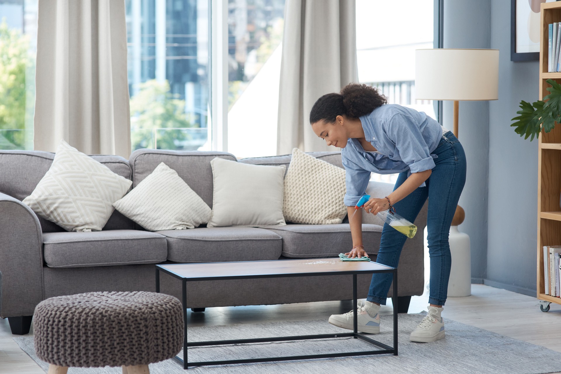 Shot of a young woman wiping down her wooden coffee table in her living room at home