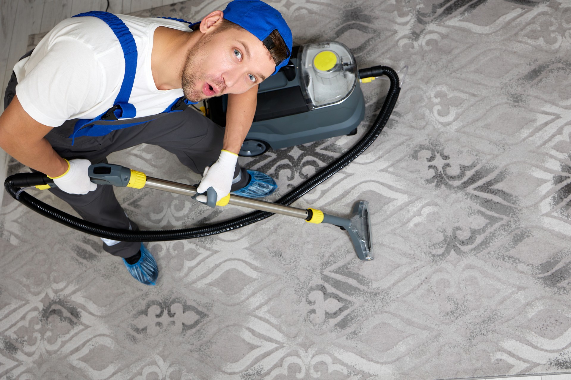 Cleaning company professional in uniform using vacuum cleaner for carpet cleaning